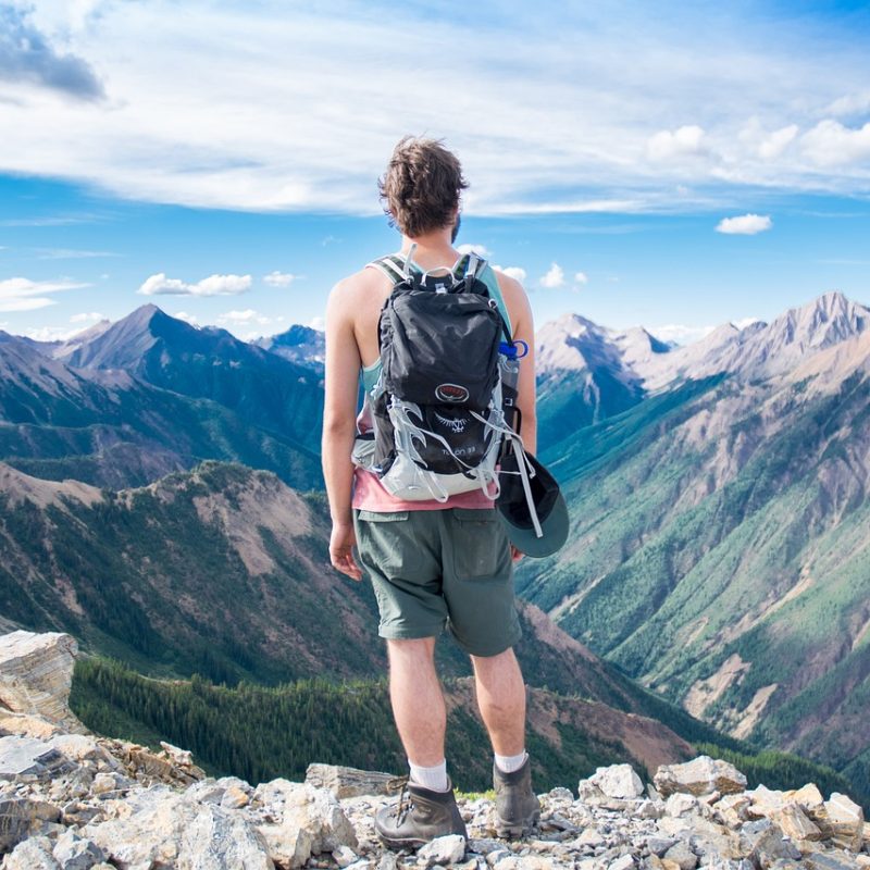 Une personne avec un sac à dos de randonneur debout au sommet d'une montagne, illustrant des conseils pour voyager à moindre coût