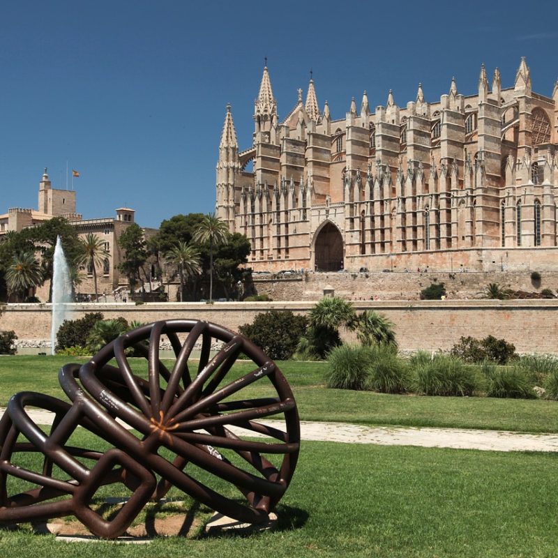 Vista de un jardín con la catedral de Palma de Mallorca al fondo, destacando la arquitectura y el diseño de la ciudad