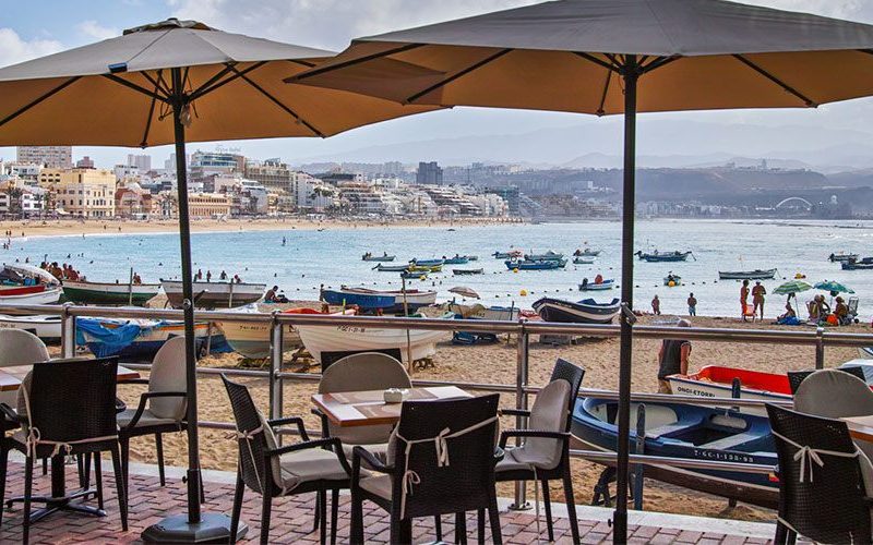 Image de l'intérieur de la terrasse d'un restaurant avec vue sur une plage de Las Palmas, où l'on voit des barques de pêche en arrière-plan