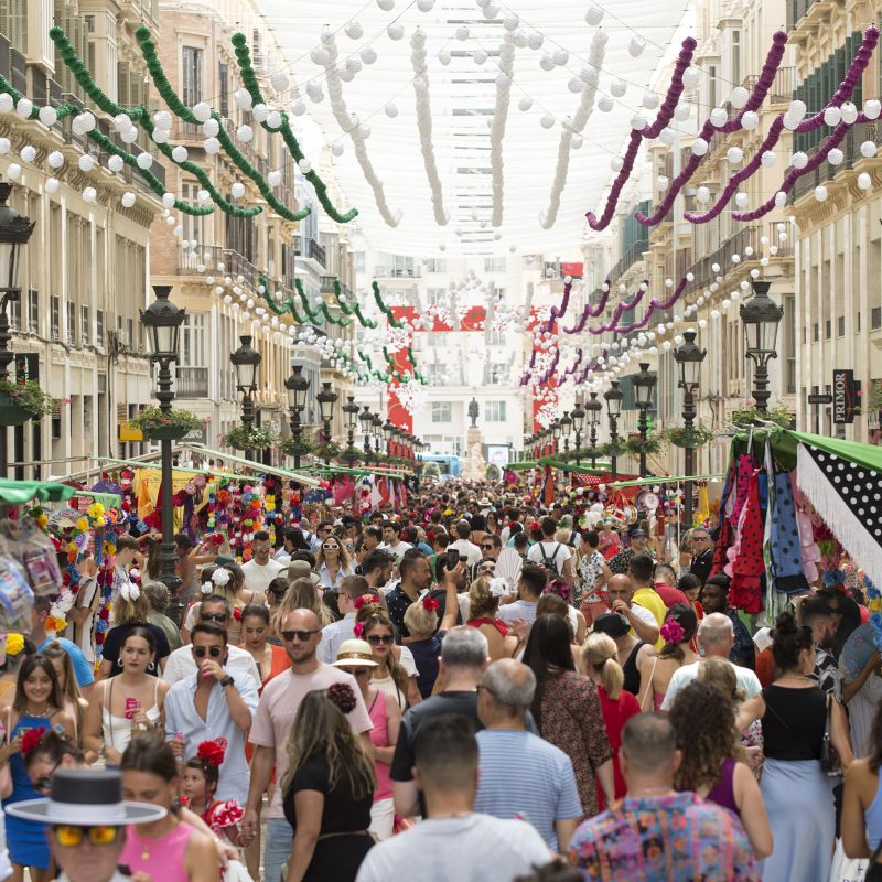 Calle Larios decorada con luces y banderines, llena de gente celebrando la Feria de Málaga