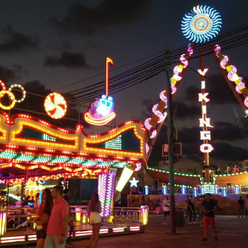 Colorful carnival rides and attractions at the Feria de Málaga, bustling with activity and illuminated with lights.