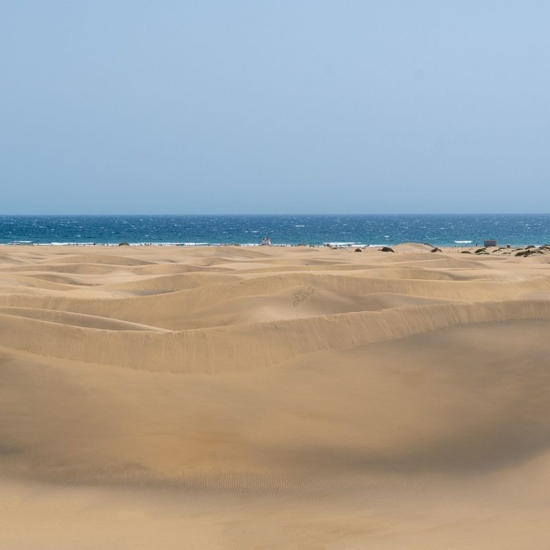 Vista panorámica de las dunas de Maspalomas con el océano Atlántico al fondo, bajo un cielo despejado