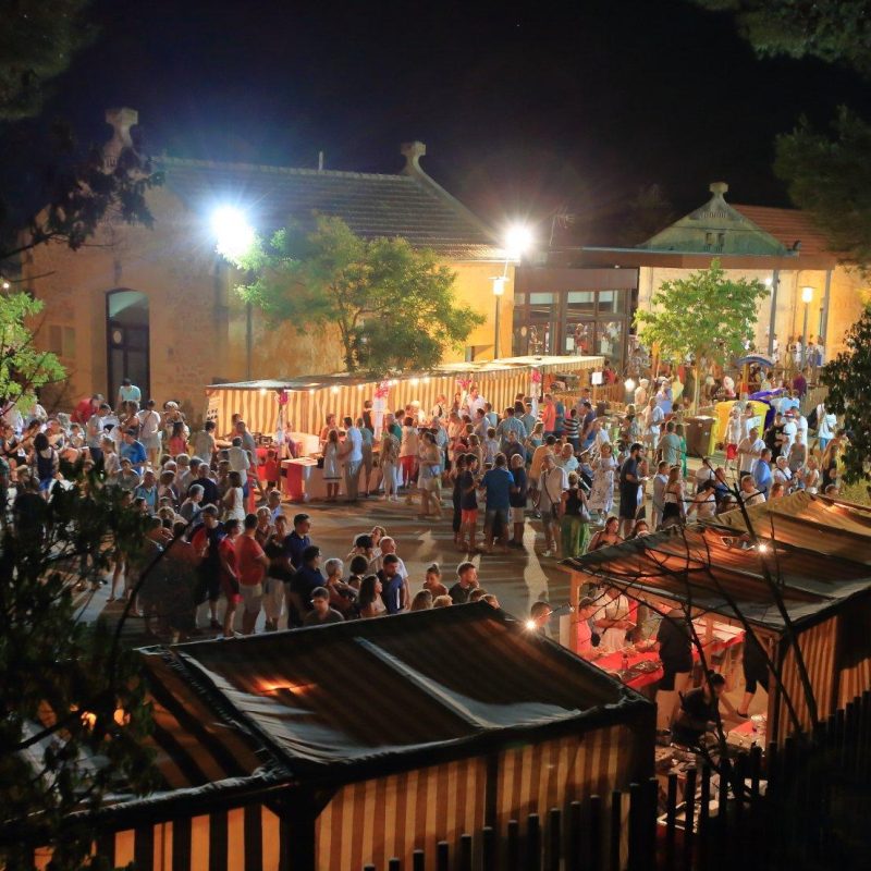 Una animada feria nocturna en Sant Llorenç, Palma de Mallorca, con luces brillantes, puestos de comida y artesanías, y una multitud de personas disfrutando del ambiente festivo en una cálida noche de agosto