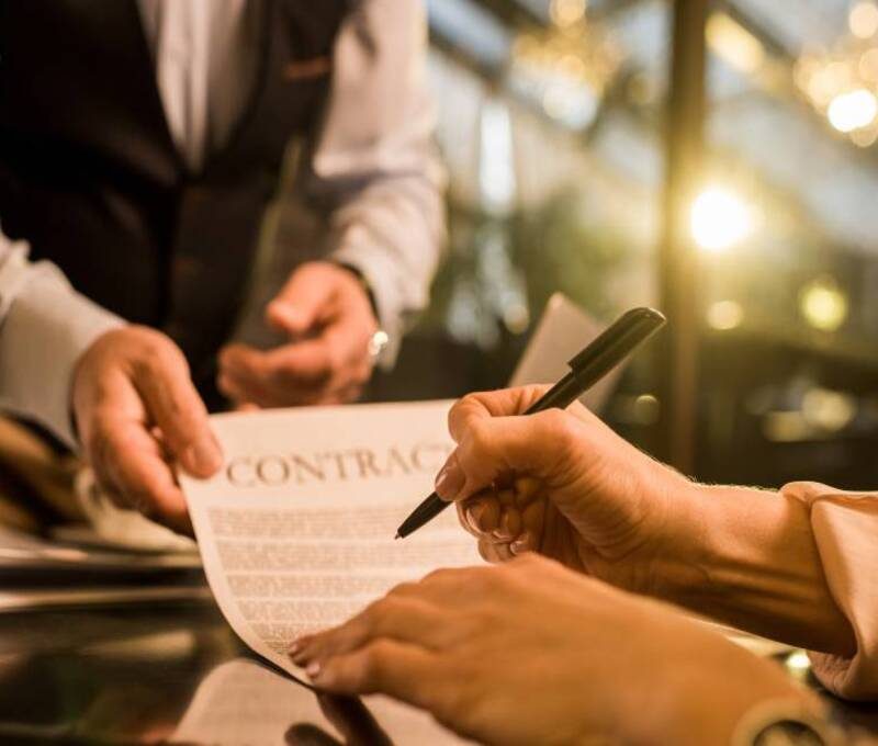 Dos personas firmando un contrato de franquicia en una mesa de oficina, con documentos y bolígrafos visibles