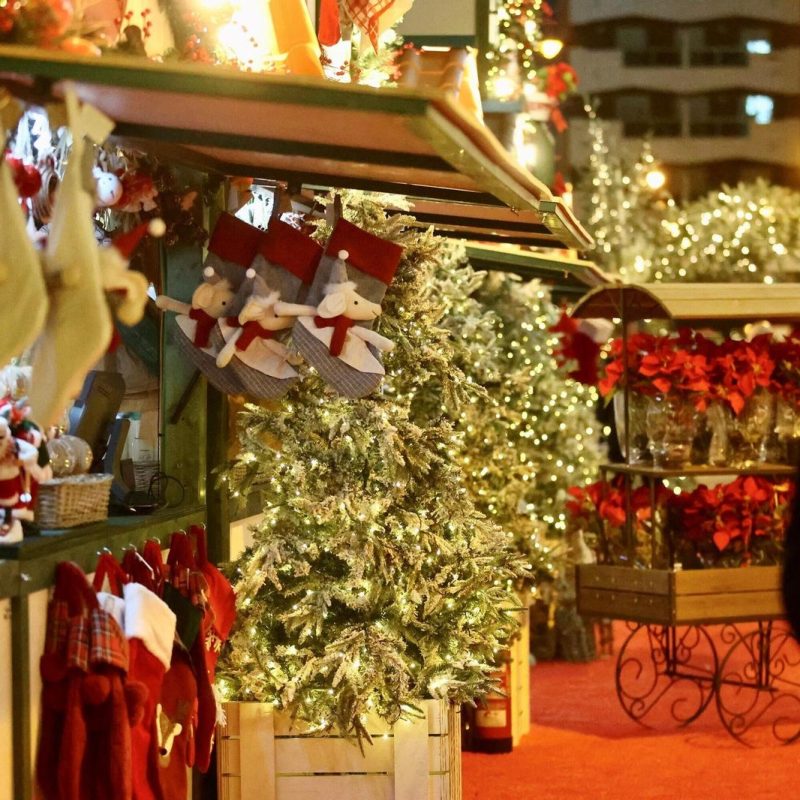 Silueta de un hombre caminando por un mercadillo navideño en Málaga, rodeado de luces y ambiente festivo