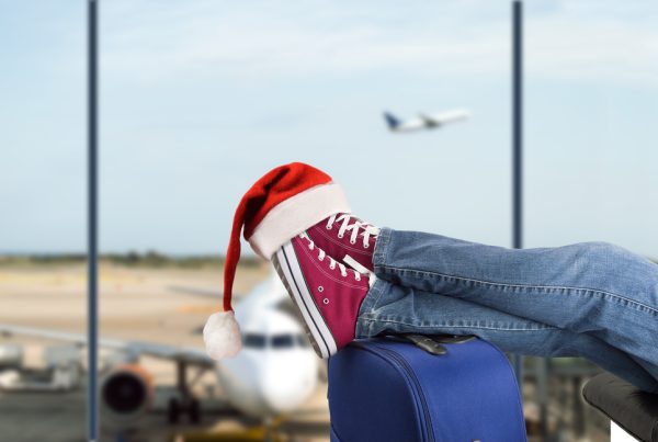 Legs resting on a suitcase with a plane in the background at an airport, symbolizing preparation for Christmas holidays