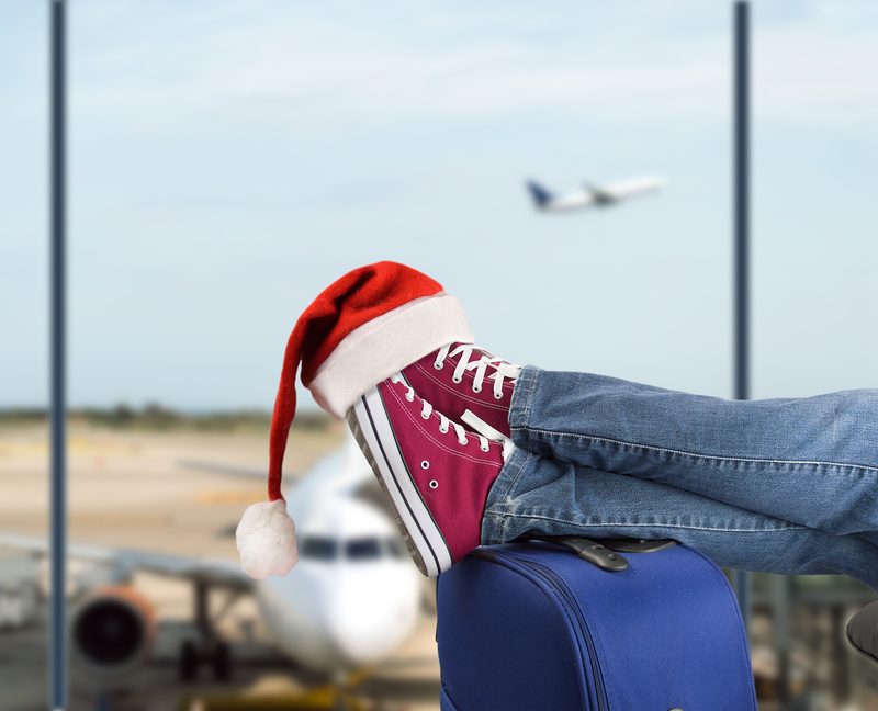 Legs resting on a suitcase with a plane in the background at an airport, symbolizing preparation for Christmas holidays