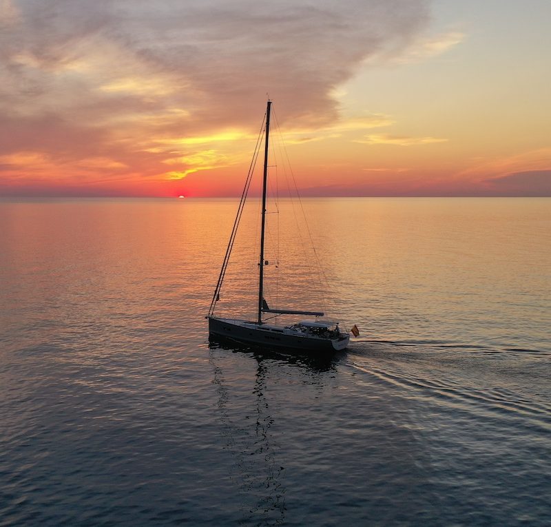 Boat sailing on the sea at sunset in Palma de Mallorca, with golden and orange hues in the sky