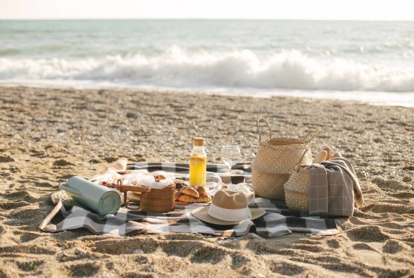 Pícnic romántico al atardecer en la playa de El Saler, Valencia, con mantas, frutas y bebidas sobre la arena