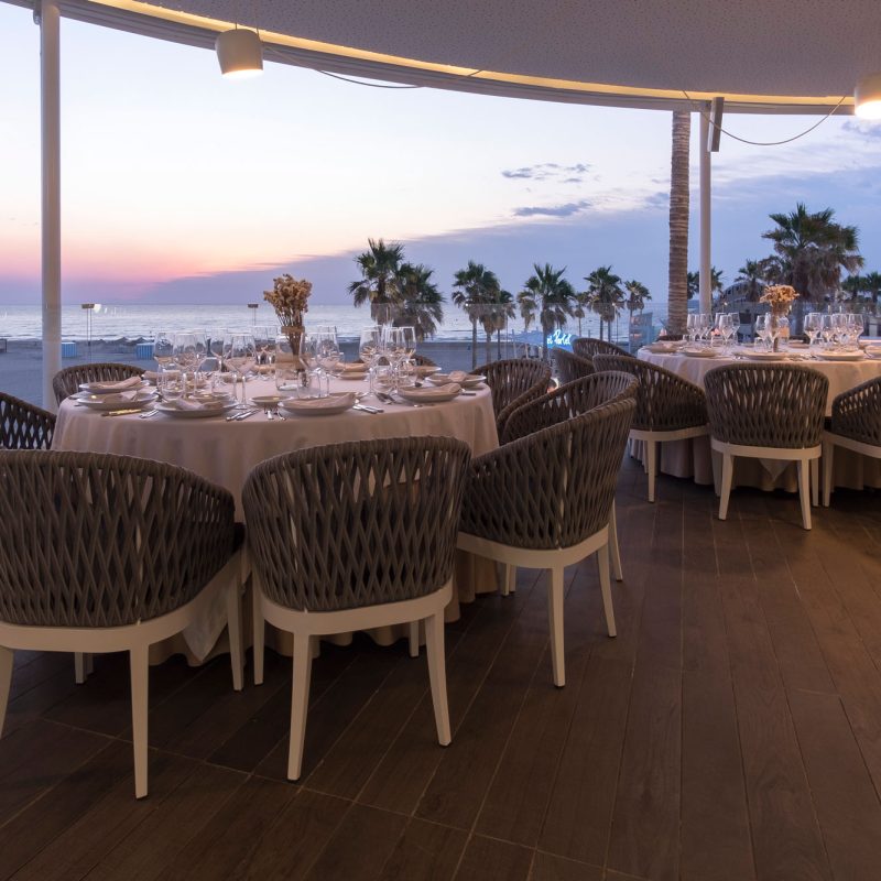 Interior of a seaside restaurant in La Marina de Valencia, with elegant tables set and panoramic views of the sea at sunset