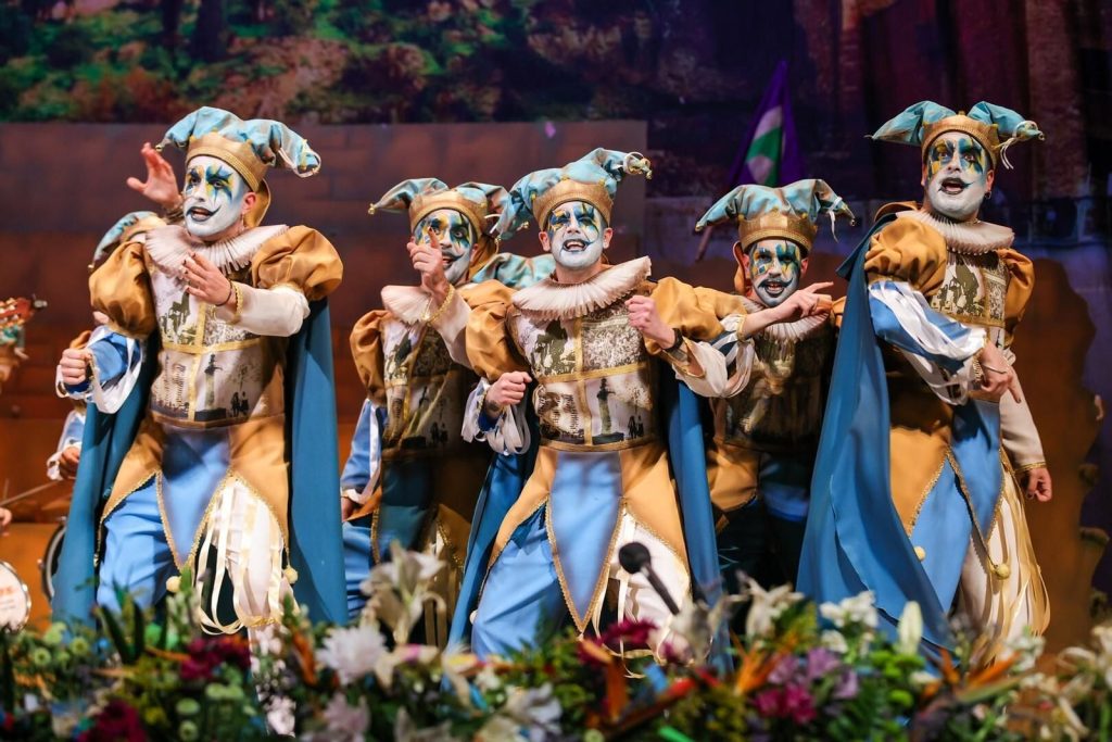Carnival group performing on stage during the Málaga Carnival, with traditional costumes and colorful makeup